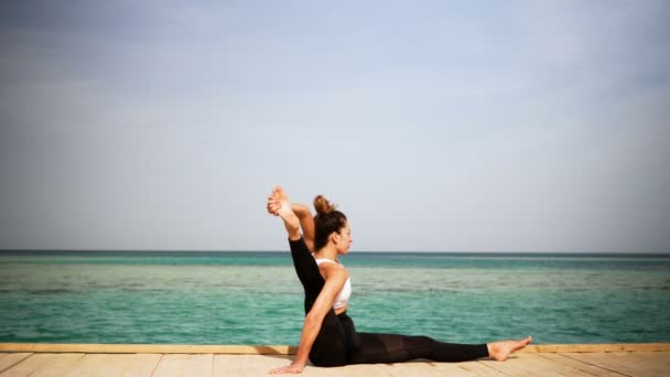 Kızı ada sahilde poz yoga yapıyor. Statik. Deniz ya da okyanus mutlu kadın gevşeme. Su ve bulutlar. El ve mavi gökyüzü. — Stok video