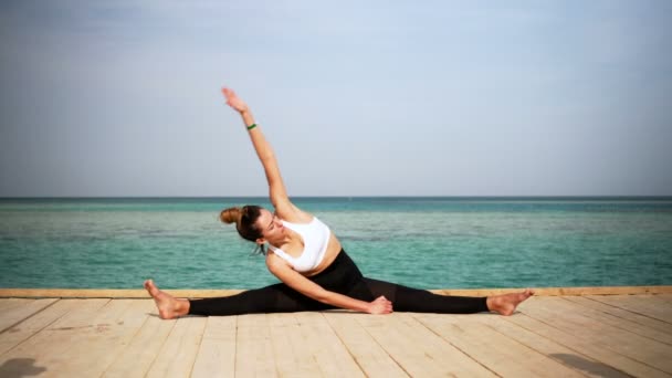 La chica está haciendo pose de yoga en la playa de la isla. Estática. Mar o océano feliz mujer relajación. Agua y nubes. Manos y cielo azul . — Vídeo de stock