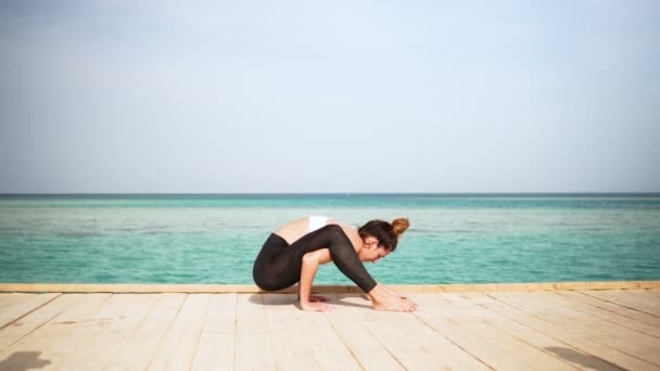 Flickan gör yoga poserar på stranden på ön. Statisk. Havet eller ocean lycklig kvinna avkoppling. Vatten och moln. Händer och blå himmel. — Stockvideo