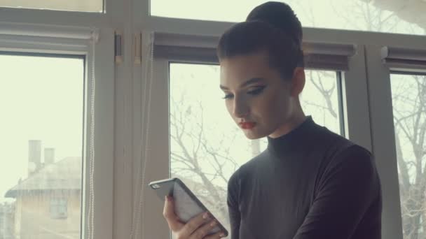 Chica bonita con teléfono inteligente. Joven mujer de negocios utilizando el teléfono de pantalla táctil en el fondo de la ciudad ventana. Personas, tecnología, conexión . — Vídeo de stock