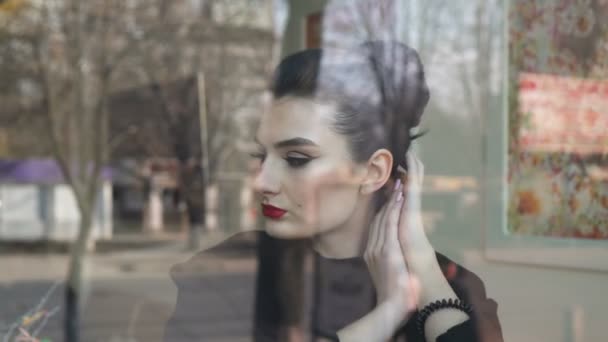 Молодая женщина смотрит через окно в кофейне. Она выглядит счастливой. Мы видим движение и людей в отражении окна . — стоковое видео