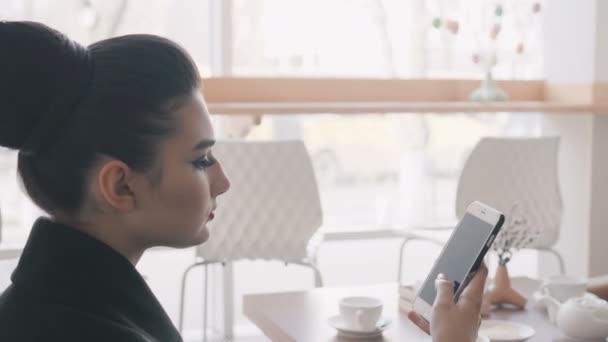 Mujer usando la aplicación en el teléfono inteligente en la cafetería bebiendo café sonriendo y mensajes de texto en el teléfono móvil. Hermosa joven multicultural casual profesional femenina en el teléfono móvil. Mezcla de raza asiática modelo caucásico . — Vídeos de Stock