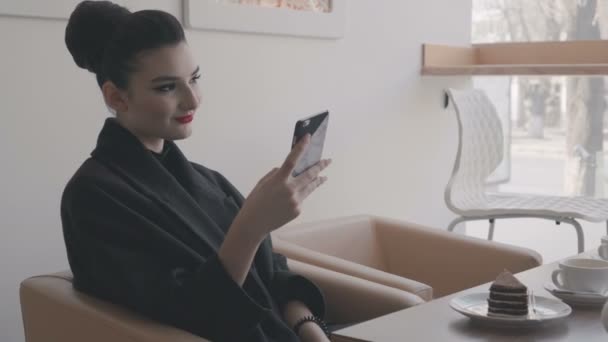 Un matin, une belle femme élégante mange le petit déjeuner au café avec un café et des croissants tout en appelant ses amis au téléphone et rit heureux.Concept : Petit déjeuner, détente, café, affaires — Video