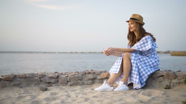 Attraente donna in cappello e vestito è seduto e guardando il tramonto — Video Stock