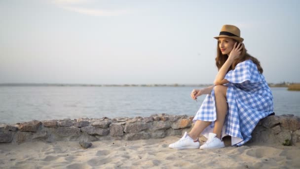 Attraente donna in cappello e vestito è seduto e guardando il tramonto — Video Stock