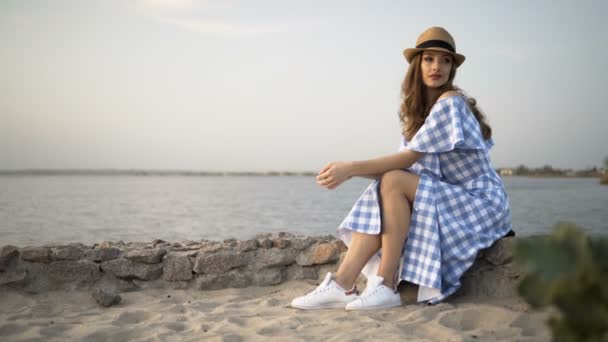 Attraente donna in cappello e vestito è seduto e guardando il tramonto — Video Stock