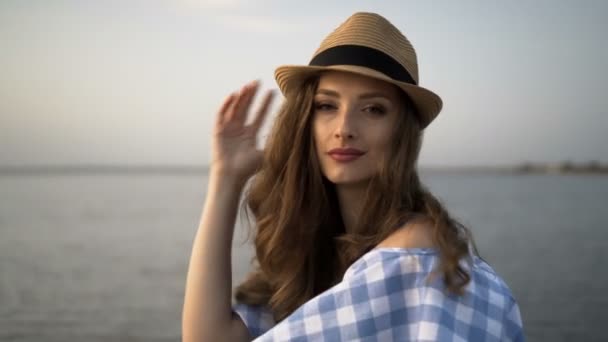 Κοντινό πλάνο. Ελκυστική γυναίκα με καπέλο και φόρεμα κάθεται και ψάχνει στο ηλιοβασίλεμα — Αρχείο Βίντεο