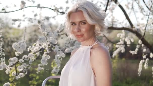 Chica y cereza floreciente. La chica está de pie estilo de vida en la naturaleza floreciendo cerezo jardín — Vídeos de Stock