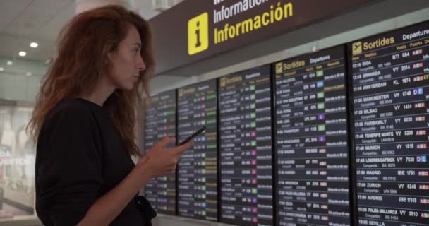 空港でスマートフォンを使う女性。若いですcaucasian旅行チェック搭乗時間とともに携帯電話アプリで端末. — ストック動画