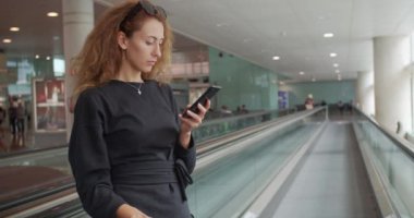 Havaalanında akıllı telefon kullanan genç bir kız. Bagajlı mutlu Avrupalı kadın terminalde cep telefonu kullanıyor.