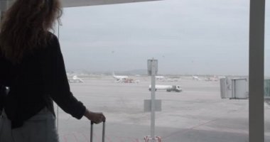 Bagajlı kadın uçağı görmek için havaalanı penceresine gider..