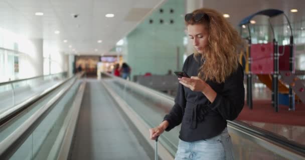 국제 공항에서 여성 이 에스컬레이터를 타고 여행 가방을 들고 휴대폰을 사용하는 모습. — 비디오