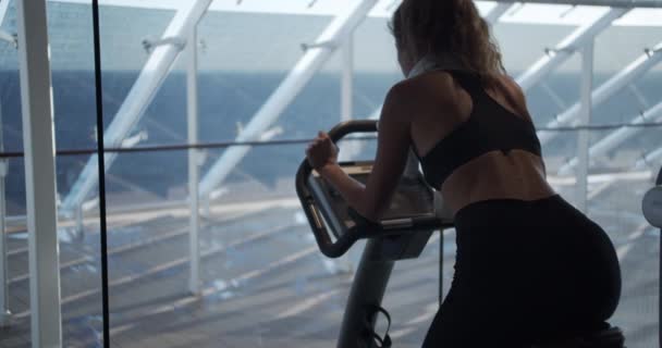 Joven hermosa chica en el gimnasio, piernas en el simulador de ciclismo. El concepto: amar los deportes, asistir a un gimnasio, una nutrición adecuada, un cuerpo delgado, estar sano . — Vídeo de stock