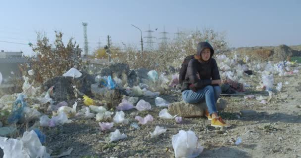 Дівчина сидить у місці, забрудненому пластиковими пакетами. Масштаби забруднення планети вражають . — стокове відео