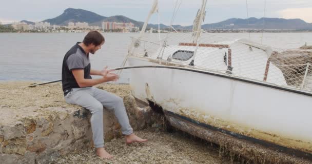 El hombre se sienta desesperado cerca de su yate roto después de una tormenta . — Vídeos de Stock