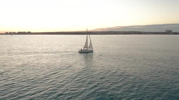 Légi felvétel. A jacht napnyugtakor vitorlázik a tengeren. Drón repül körbe a jachton vitorlákkal. — Stock videók