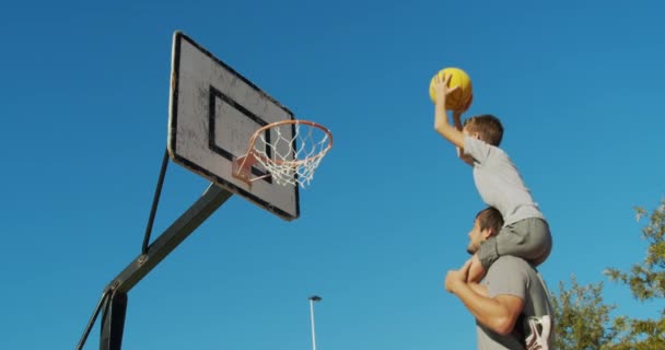 Vater und Sohn spielen Basketball auf der Straße und werfen einen Ball in den Korb. — Stockvideo