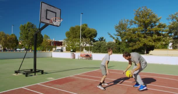 Vader en zoon spelen basketbal op straat en gooien een bal naar de basket. — Stockvideo