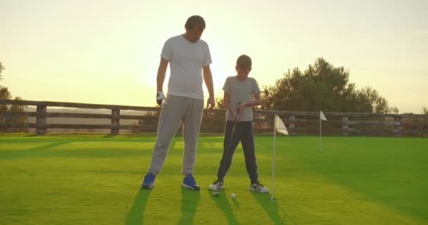 Чоловік з сином грає в гольф на ідеальному полі для гольфу в літній день . — стокове відео