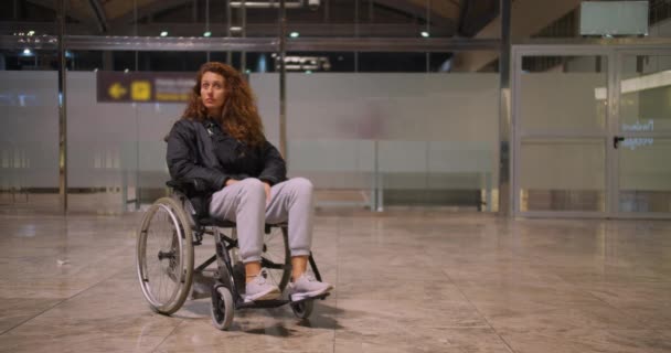 Joven mujer discapacitada en silla de ruedas en un aeropuerto. Ella está sola y mirando a su alrededor . — Vídeo de stock