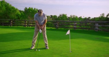 Yakışıklı yaşlı golfçü gün batımında golf sahasında sallanıyor ve vuruyor..