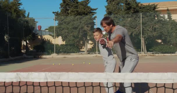 Niño entrando en el tenis. Padre e hijo practican golpes en el tenis con coart. Ocio activo juntos . — Vídeos de Stock