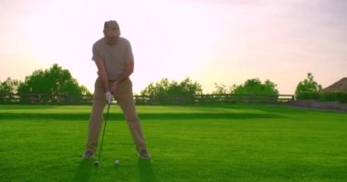 Yakışıklı yaşlı golfçü gün batımında golf sahasında sallanıyor ve vuruyor..