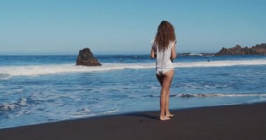 Okyanus boyunca yürüyen bir kız. Sahilde okyanusa bakan beyaz bir kadının arka görüntüsü..