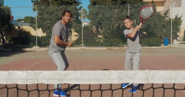 Niño entrando en el tenis. Padre e hijo practican golpes en el tenis con coart. Ocio activo juntos . — Vídeos de Stock