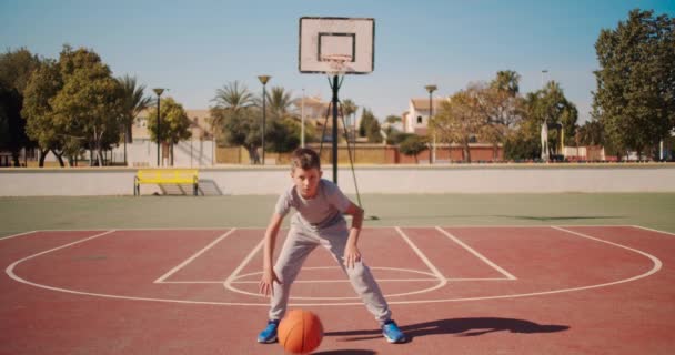 Roztomilý kluk, co odpaluje basketbal. Chlapec cvičí střelbu na basketbal. — Stock video