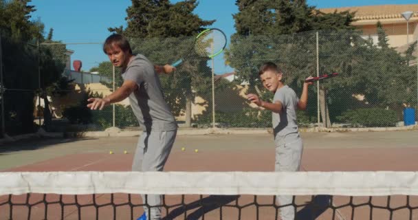Dziecko trenujące tenisa. Ojciec i syn ćwiczą uderzenia w tenisa na coart. Wspólny aktywny wypoczynek. — Wideo stockowe