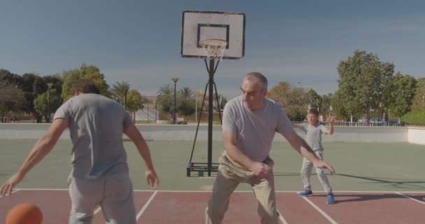 Flergenerationens familj spelar basket på friluftsplan. — Stockvideo