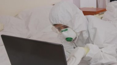 Koruyucu giysili bir çocuk ve salgın sırasında izole edilmiş bir bilgisayarın başında solunum cihazı..