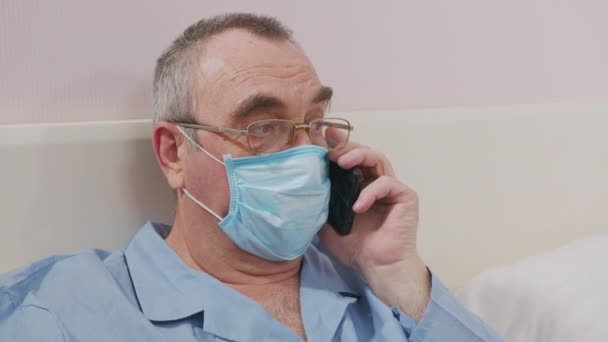 Больной человек в постели разговаривает в маске по телефону . — стоковое видео