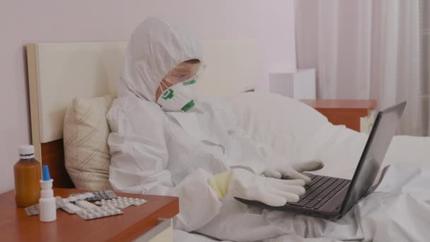 Un băiat într-un costum de protecție și un aparat respirator acasă la un computer izolat în timpul unei epidemii . — Videoclip de stoc