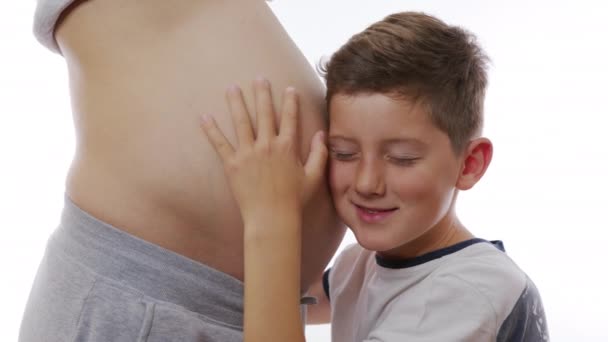 Zblízka velké těhotné břicho a malý chlapec se ho dotýká. Bílé pozadí stěny. — Stock video