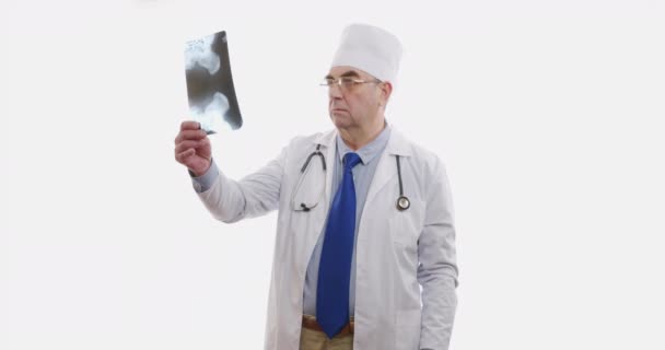 Mužský doktor vyšetřuje rentgen a drží ho v rukou uvnitř. Zkušený expert oblečený v bílém. Izolováno na bílém, 6k. — Stock video