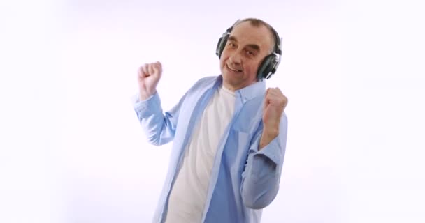 Movimiento lento de feliz anciano hombre en auriculares inalámbricos bailando disfrutando de la música. Dispositivos modernos, estilo de vida y concepto de salud . — Vídeo de stock