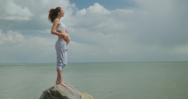 Беременная женщина гладит живот на берегу моря . — стоковое видео