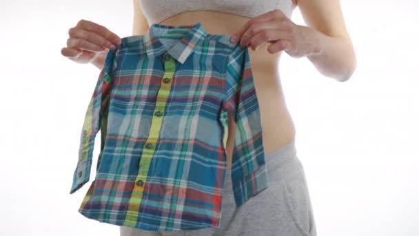 Mulher grávida feliz aplica roupas de bebês para bebê da barriga. Maternidade, gravidez, pessoas e crianças conceito de vestuário. Fechar, 6K . — Vídeo de Stock