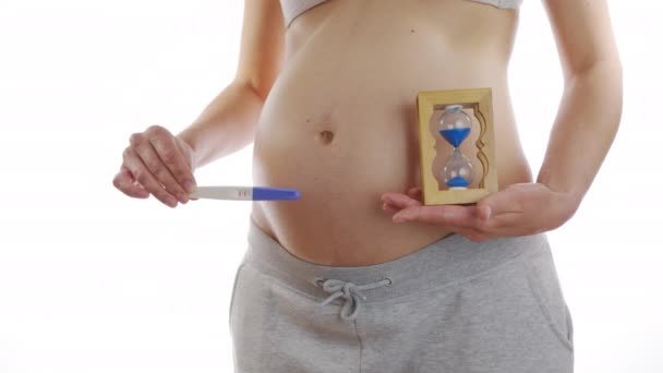 Flickan på buken visar ett positivt graviditetstest och ett timglas. Begreppet snabb tid som visas i graviditeten. Närbild, 6k. — Stockvideo
