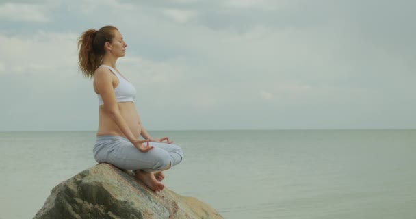 Ung kvinna som gör yoga sittandes i lotusställning på naturen utomhus. — Stockvideo