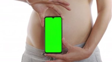 Elinde yeşil ekran akıllı telefonu olan hamile bir kız ve karnının üstünde telefon kullanıyor. Yakın çekim, 6k.