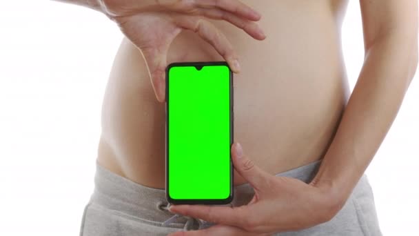 Беременная девушка держит смартфон с зеленым экраном и водит телефон на животе. Крупный план, 6k . — стоковое видео