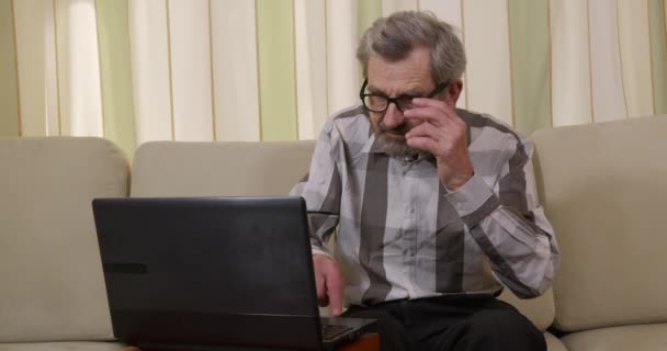 Abuelo en gafas ocupadas cerca de la computadora portátil, mirando la pantalla y escribiendo . — Vídeos de Stock