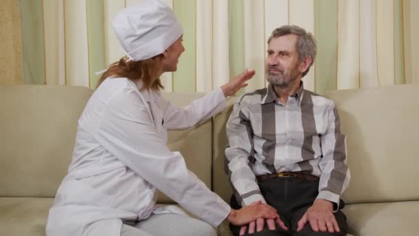 Жінка-лікар заспокоює старшого дідуся вдома . — стокове відео