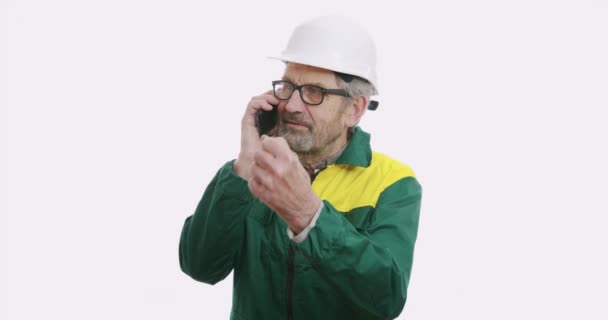 Portret van een oude zakenman in pak en helm geïsoleerd over een witte achtergrond aan de telefoon. — Stockvideo