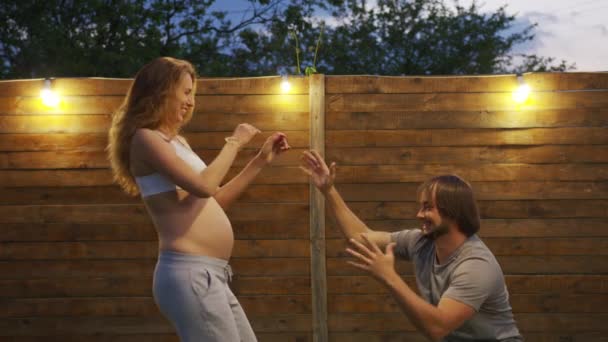 A pregnant woman is dancing with her husband in the backyard of her house. Couple waiting for baby. — Stock Video