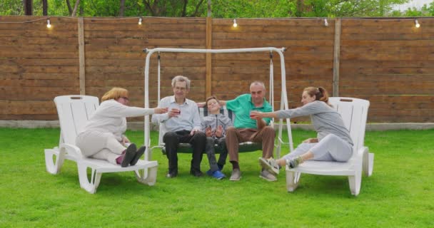 Een groot familiefeest in de tuin. Mensen zijn aan het drinken, passeren borden, grappen maken en plezier hebben. — Stockvideo