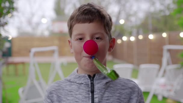 Jongen in grappige kleurrijke kostuum in viering met een rode neus en een feestelijke pijp. Vakantie concept, verjaardag. — Stockvideo